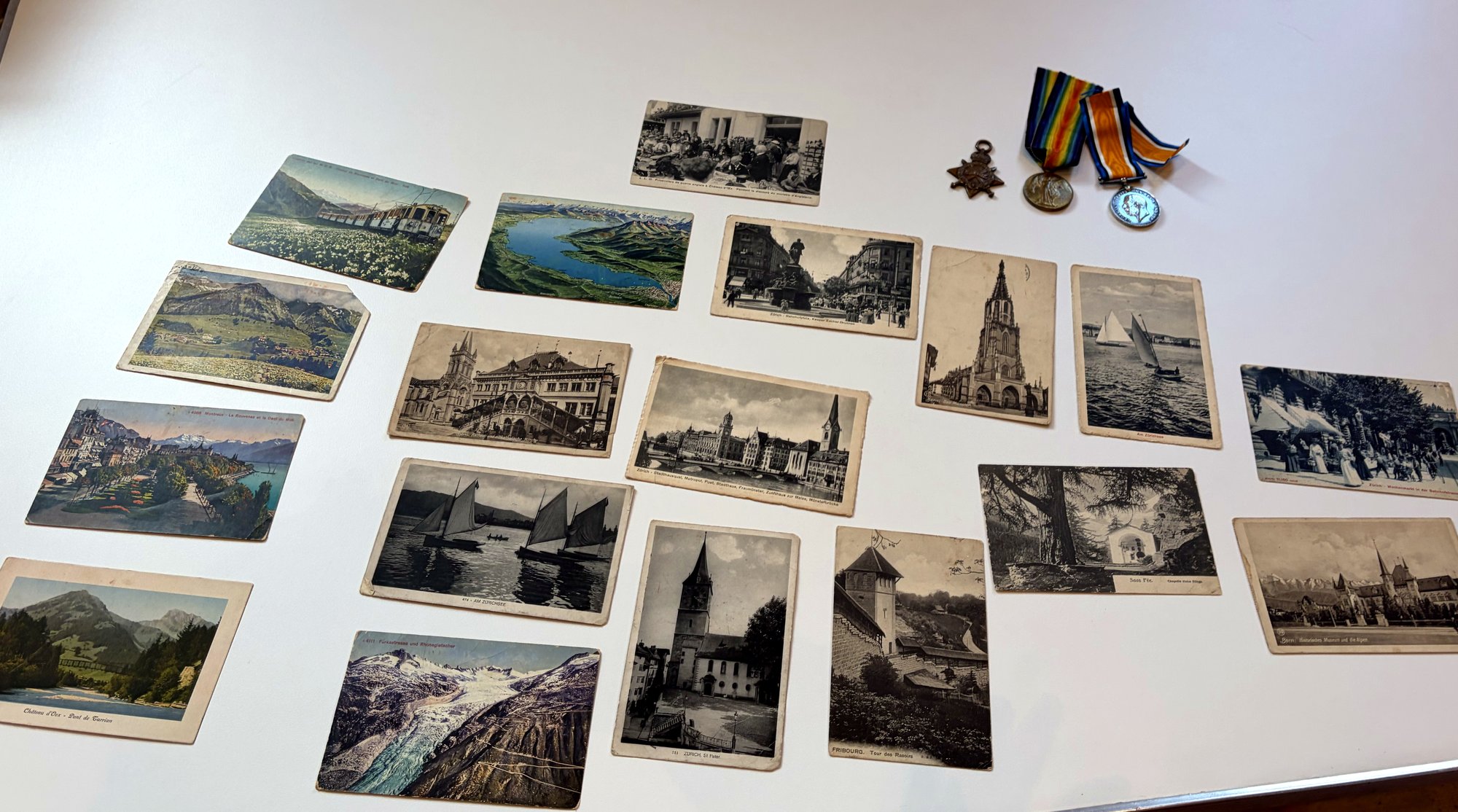 Fourteen First World War postcards laid out on a table beside three campaign medals