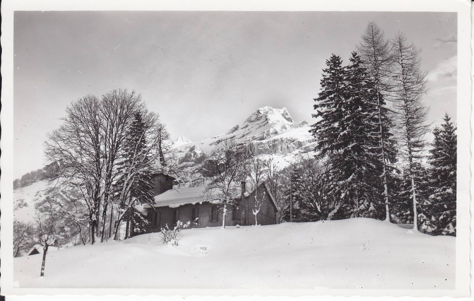 The English church at Les Diablerets in deep winter snow, among tall trees, with the Diablerets massif behind