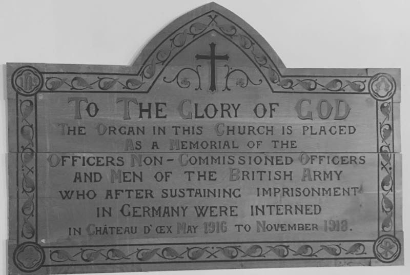 A carved wooden plaque with a cross at its apex, lettered: To the glory of God, the organ in this church is placed as a memorial of the officers, non-commissioned officers and men of the British Army who after sustaining imprisonment in Germany were interned in Château d'Œx, May 1916 to November 1918