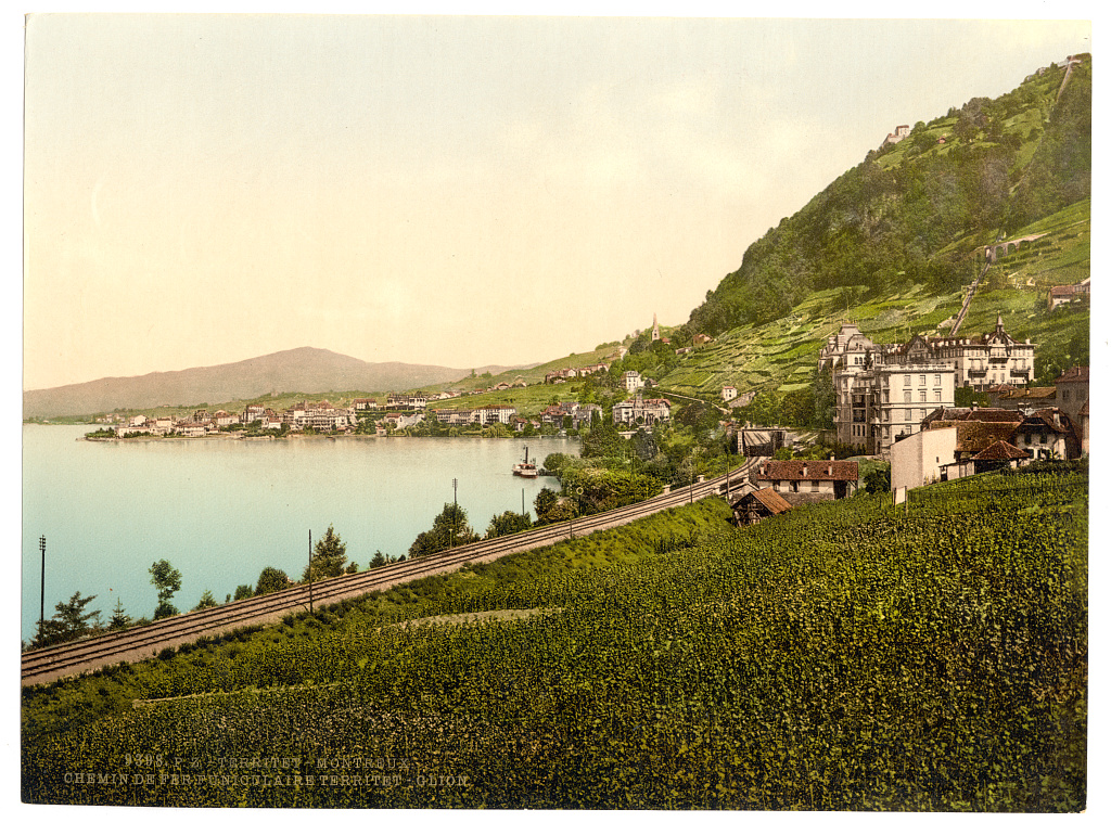 Railway tracks curving through vineyard terraces above the lake at Territet, with a large hotel on the hillside and a steamer on the water